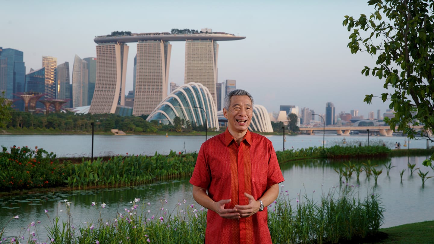 Lee Hsien Loong in red shirt, Marina Bay Sands and waterfront garden backdrop.